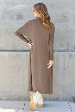 Woman wearing a Basic Bae long sleeve cover up in taupe, showcasing its sheer pocketed design and stylish silhouette.