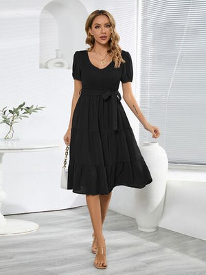 Black smocked tie front short sleeve tiered dress with a flattering silhouette and belt detail for a chic look.