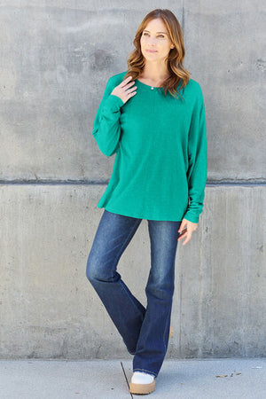 Model wearing a green long sleeve t-shirt paired with flared jeans against a concrete wall.