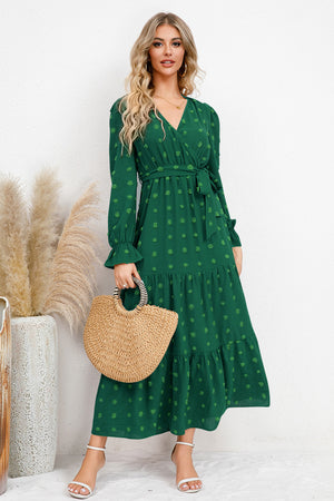 Model wearing a green Swiss Dot Tied Surplice Flounce Sleeve Dress, holding a straw bag in a bright setting.