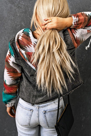 Back view of a woman in a hooded denim jacket with colorful tribal sleeves, showing long hair and casual jeans.