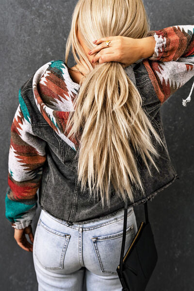 Back view of a woman in a hooded denim jacket with colorful tribal sleeves, showing long hair and casual jeans.