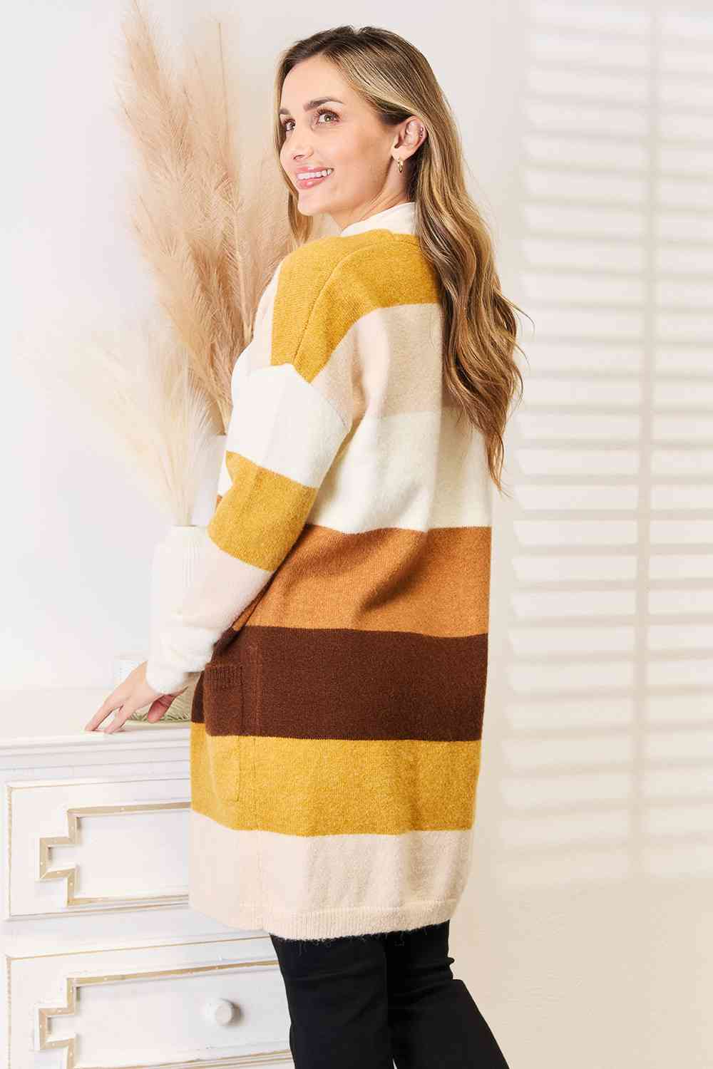 Woman wearing a color block dropped shoulder cardigan with shades of yellow, beige, and brown, featuring a cozy relaxed fit.