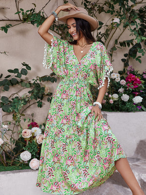 Model in a floral V-neck dress with short sleeves, styled with a hat and surrounded by flowers.