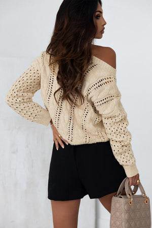 Model wearing a beige openwork cable-knit top with black shorts and a stylish handbag.