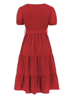 Back view of a red smocked tie front short sleeve tiered dress, showcasing a tiered skirt and puff sleeves.