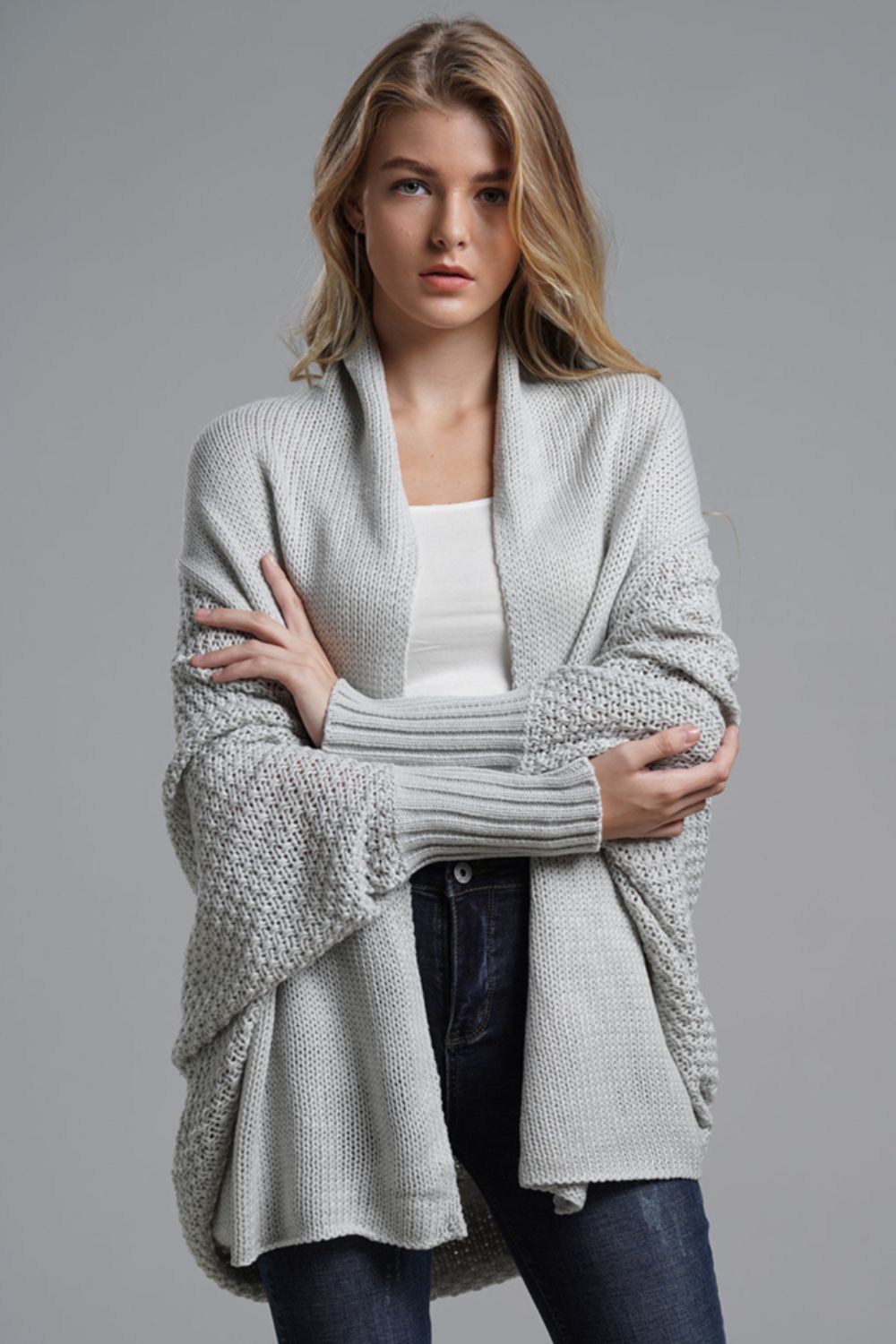 Model wearing a light grey dolman sleeve open front ribbed cardigan, styled with a white tank and jeans.