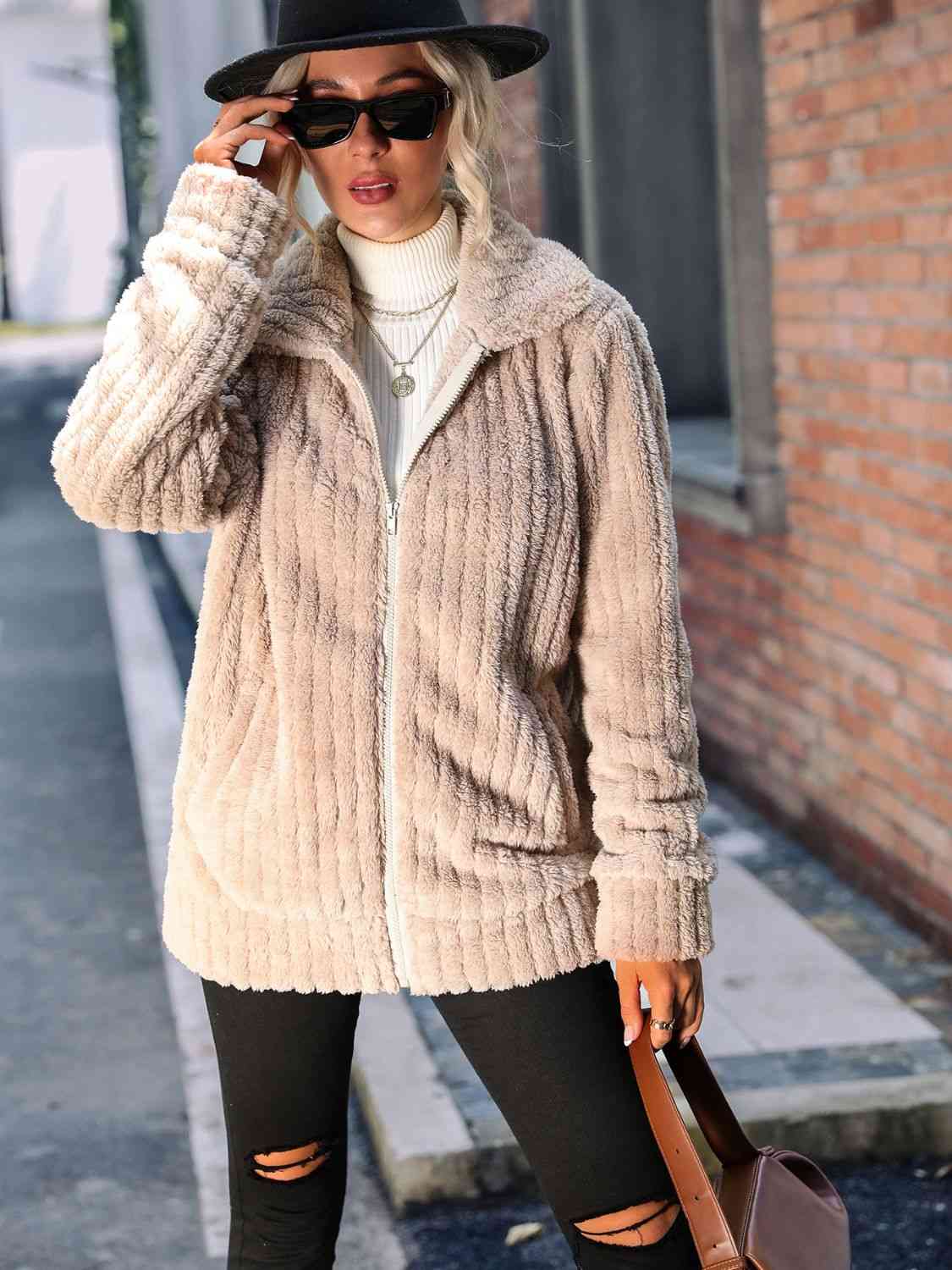 Stylish woman in a zip-up collared ribbed jacket, paired with sunglasses and a hat, showcasing urban fashion.