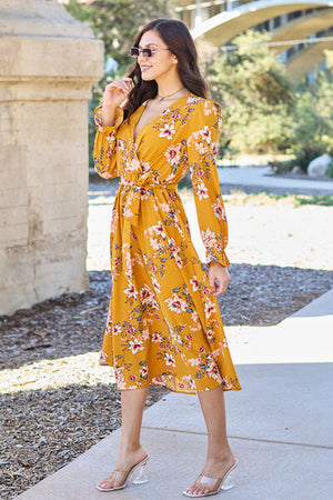 Model wearing a double take full size floral tie back flounce sleeve dress in mustard yellow, showcasing a stylish floral pattern.