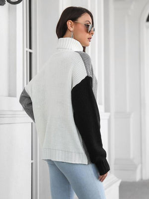 Back view of a woman wearing a contrast turtleneck long sleeve sweater with a white, gray, and black color block design.