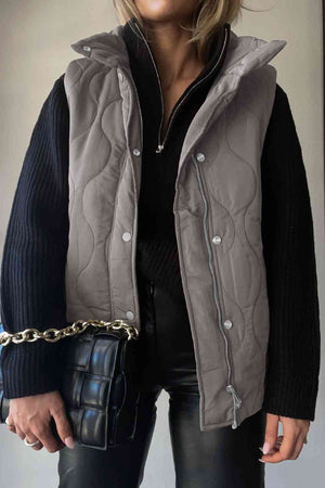 Stylish collared neck vest in gray with pockets, layered over a black sweater and paired with a chic handbag.