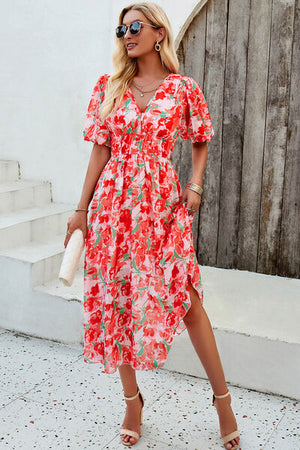 Model wearing a smocked printed V-neck short sleeve dress in floral design, posing outdoors with sunglasses.