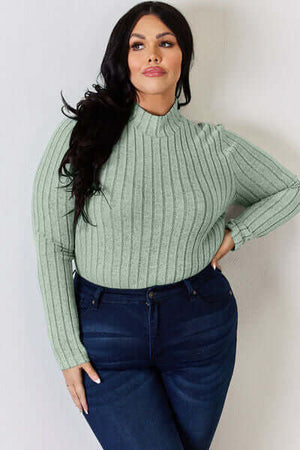 Plus size model wearing a mint green ribbed mock neck long sleeve t-shirt paired with dark jeans.