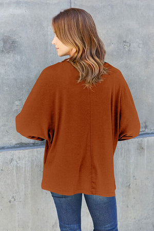 Back view of a woman wearing a rust-colored oversized top against a neutral background.