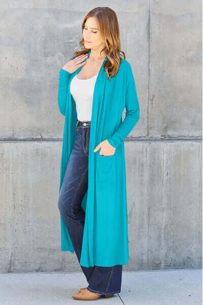 Model wearing Basic Bae turquoise long sleeve cover up with pockets, styled with a white top and jeans.