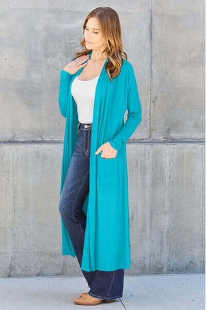 Model wearing Basic Bae turquoise long sleeve cover up with pockets, styled with a white top and jeans.