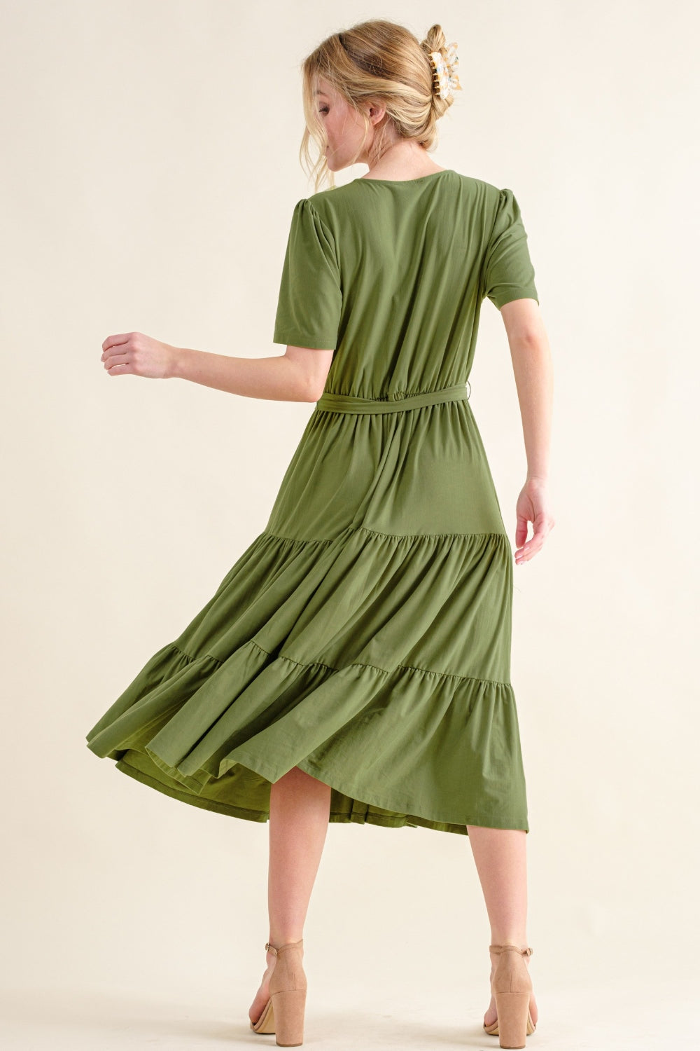 Back view of a model in a green tiered midi dress with short sleeves, showcasing a flowy silhouette.