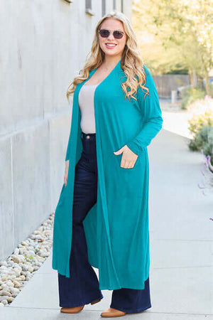 Woman wearing a teal open front long sleeve cover-up with pockets, styled with flared jeans.