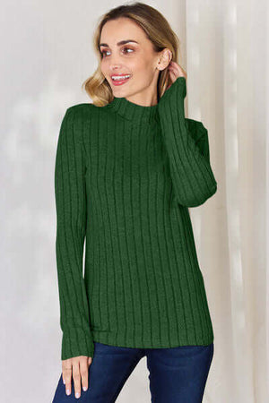 Woman wearing a green ribbed mock neck long sleeve t-shirt, smiling with a relaxed pose.