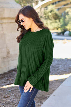 Woman wearing a dark green ribbed long sleeve knit top, paired with sunglasses, walking outdoors.
