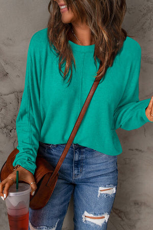 Woman wearing a turquoise long sleeve t-shirt with a relaxed fit, paired with distressed jeans and holding a drink.