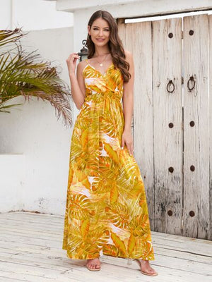 Model wearing a vibrant yellow floral printed surplice spaghetti strap dress, standing in a tropical setting.