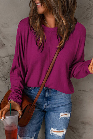 Woman wearing a purple long sleeve t-shirt with a stylish casual look, holding a drink.