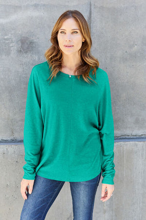 Woman wearing a vibrant green long sleeve top with a round neck against a concrete background.