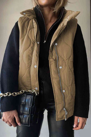 Stylish woman in collared neck vest with pockets, layered over black sweater, holding a trendy handbag.