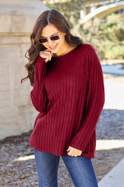 Model wearing a maroon ribbed long sleeve knit top with round neck and sunglasses, paired with jeans.