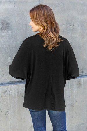 Model wearing a loose black top, showcasing a stylish back view against a concrete background.