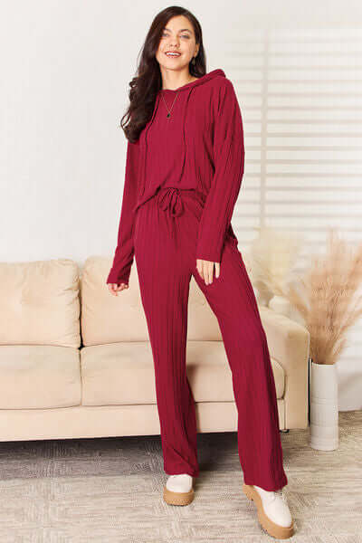 Model wearing burgundy Basic Bae ribbed hood top and pants set, showcasing cozy chic style on a sofa.