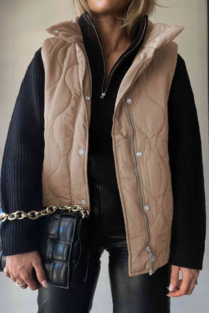 Stylish woman wearing a collared neck vest with pockets, layered over a black sweater and holding a trendy handbag.