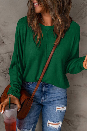 Woman wearing a green long sleeve top with a relaxed fit, styled with ripped jeans and a brown bag.