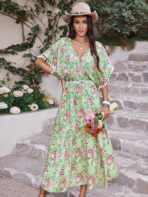 Model wearing a smocked floral V-neck short sleeve dress in green with floral print, holding a bouquet of flowers.