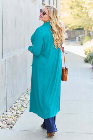 Woman in turquoise long sleeve cover-up walking outdoors, showcasing a stylish pocketed design.
