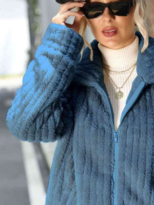 Woman wearing a stylish blue zip-up collared jacket over a turtleneck, accessorized with sunglasses.