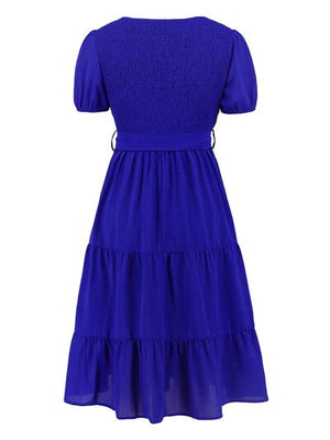 Back view of a smocked tie front short sleeve tiered dress in vibrant blue, featuring a tiered skirt and puff sleeves.