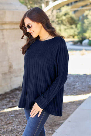 Woman wearing a navy ribbed long sleeve knit top with round neck, styled with jeans outdoors.