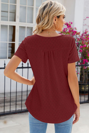 Back view of a woman in a rust eyelet quarter button short sleeve t-shirt, paired with light blue jeans.
