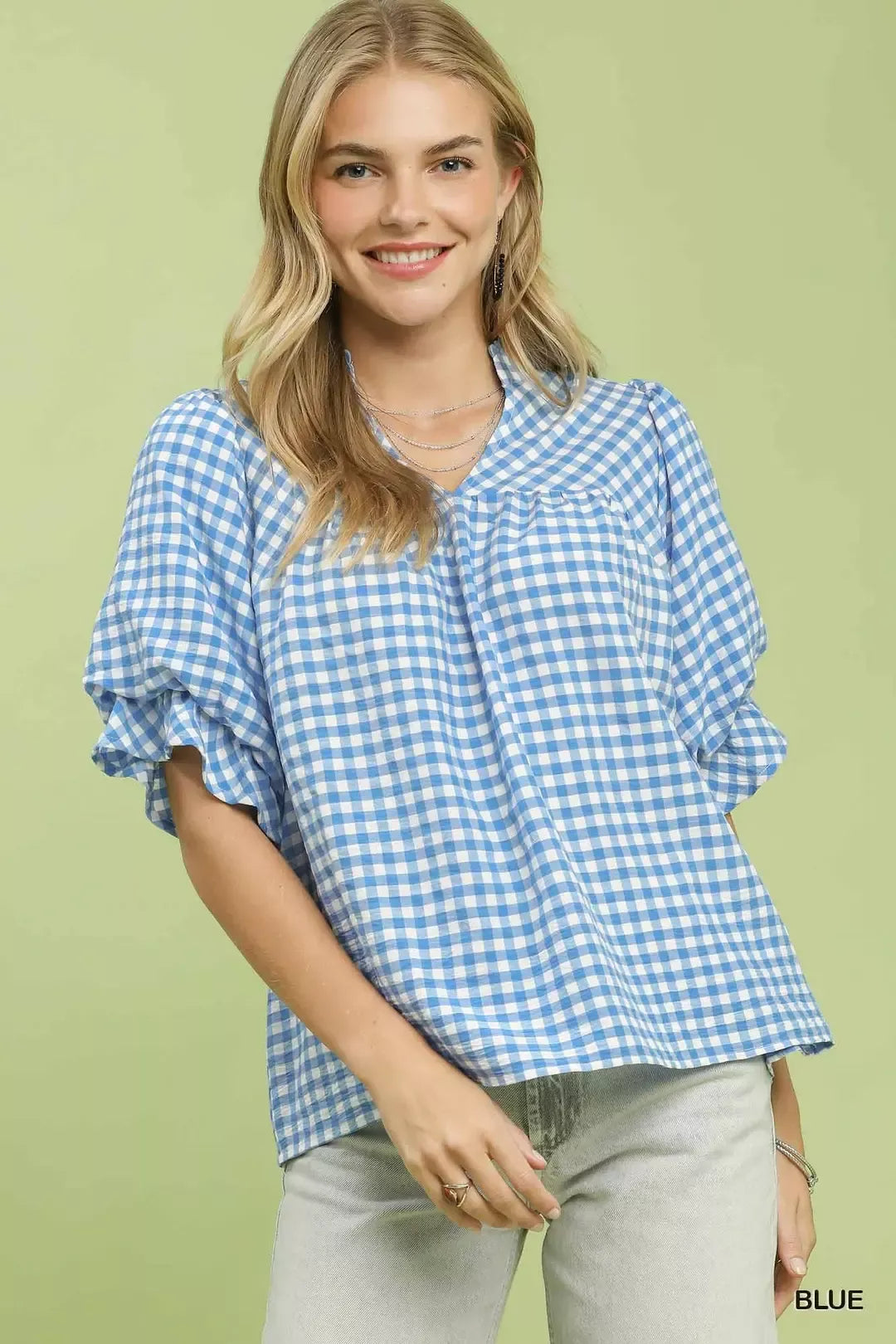 Umgee Gingham Check Blouse with Ruffle Sleeves in blue worn by a smiling woman against a green background.