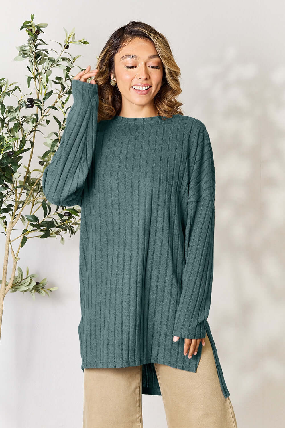 Model wearing a ribbed round neck long sleeve top in teal, featuring side slits and a relaxed fit.