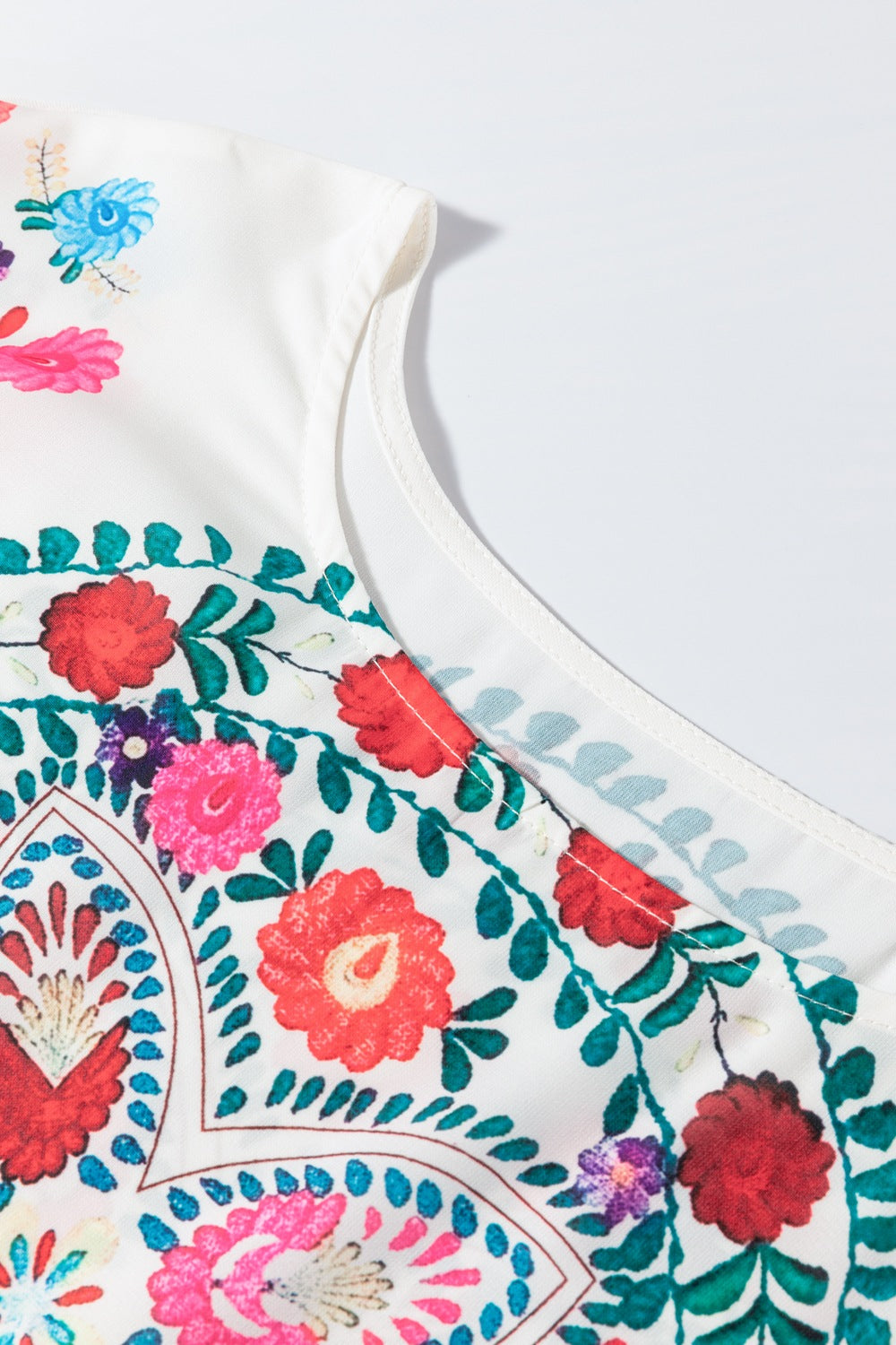 Close-up of floral print fabric on round neck blouse with ruffle trim, showcasing vibrant embroidery details.