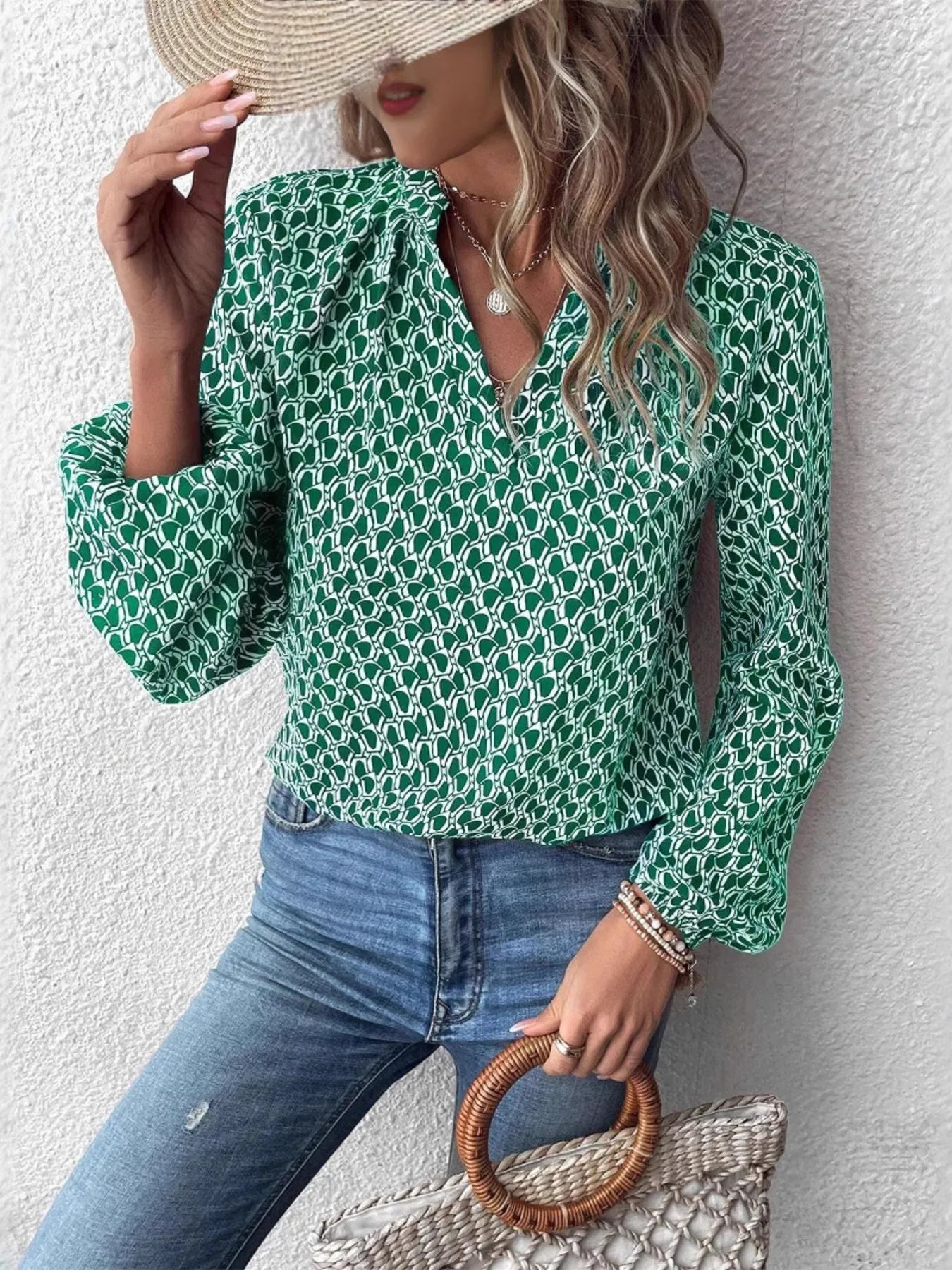 Woman wearing a green printed notched long sleeve blouse, paired with denim jeans and a stylish hat.