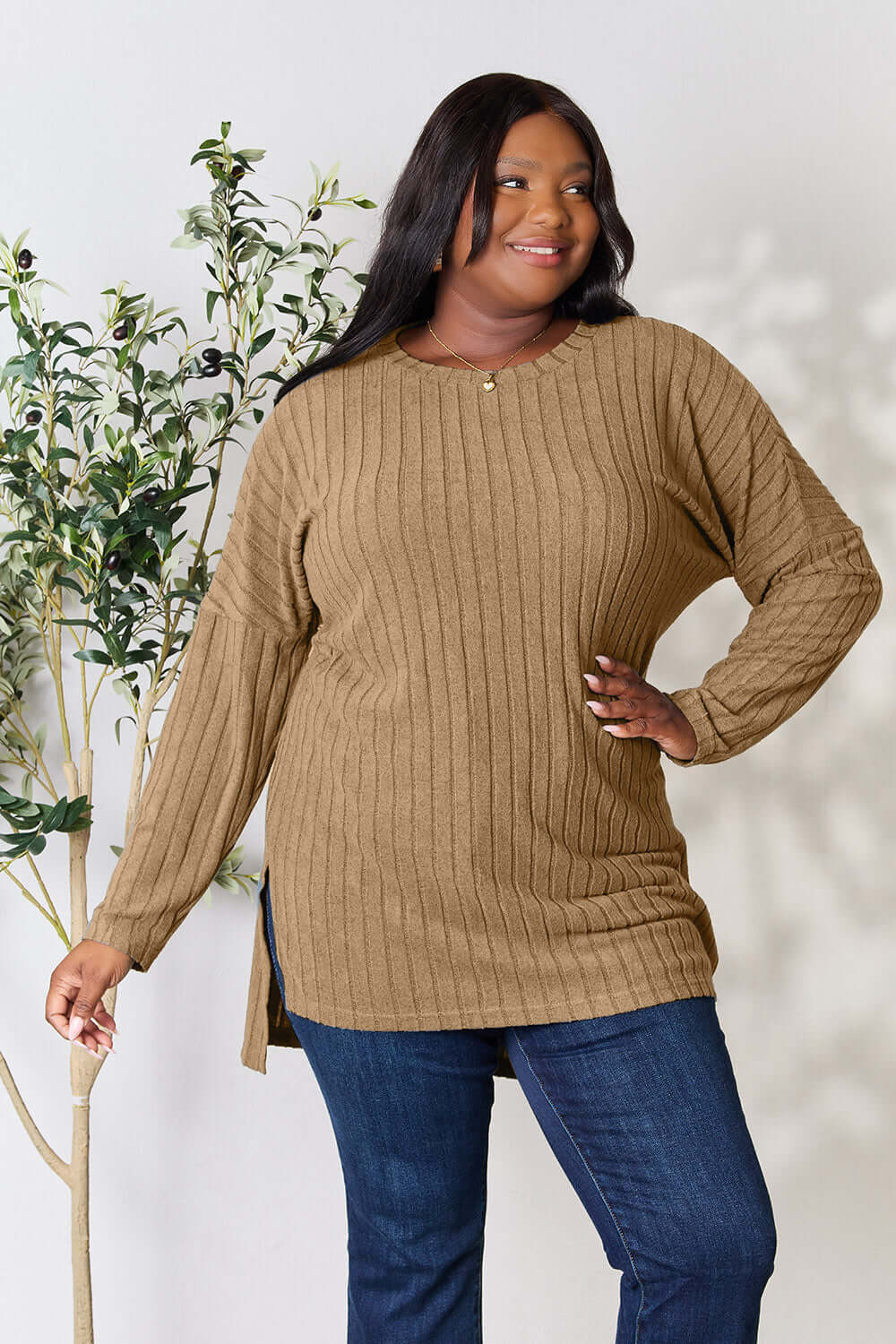 Plus-size model wearing a ribbed, high-low, long sleeve, brown top with side slits against a neutral background.