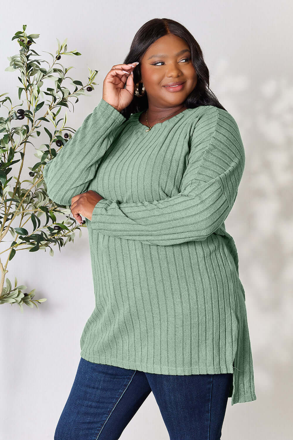 Model in a plus-size ribbed green long sleeve slit top paired with jeans, showcasing a stylish high-low design.