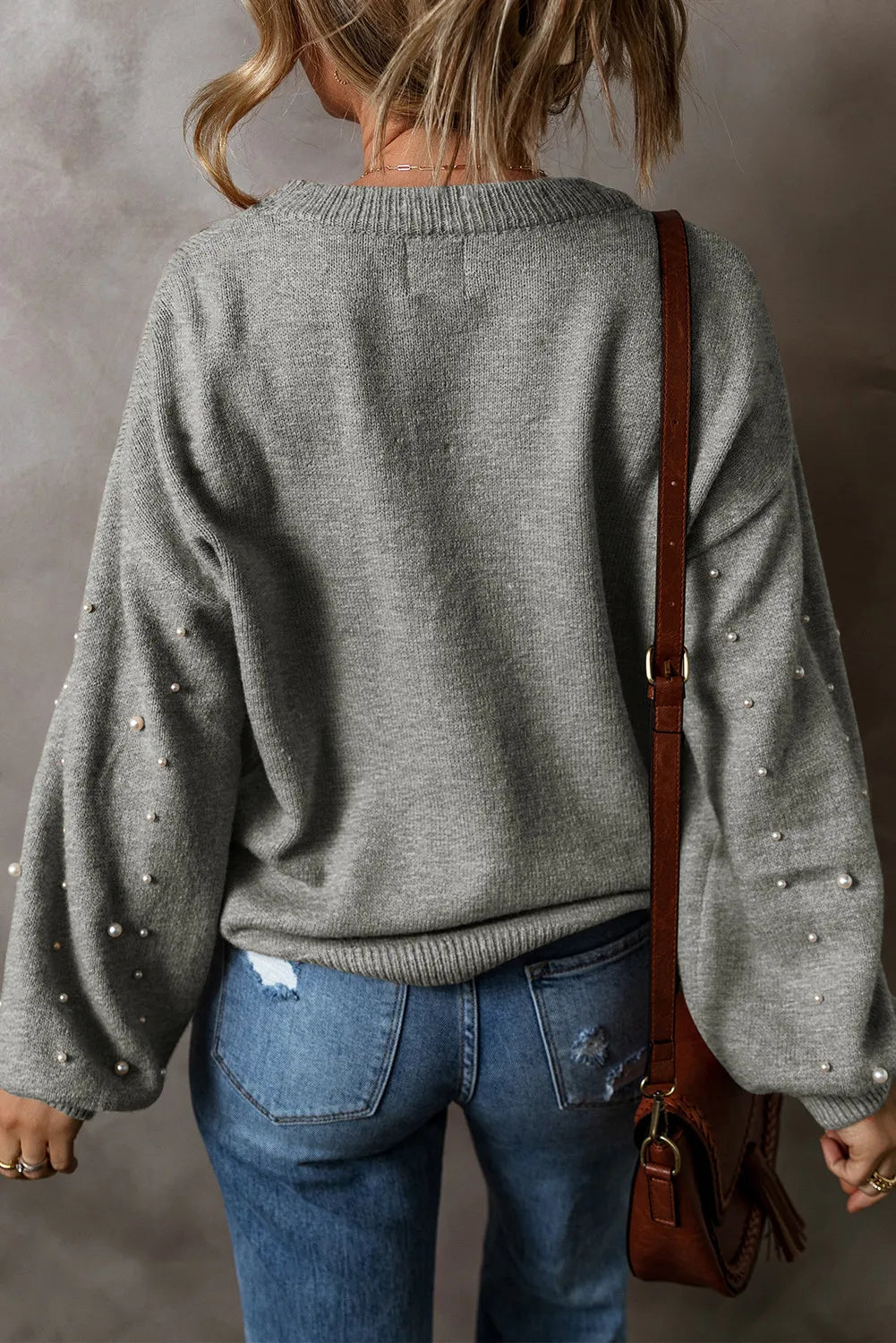 Back view of a grey pearl detail long sleeve sweater paired with jeans and a shoulder bag.