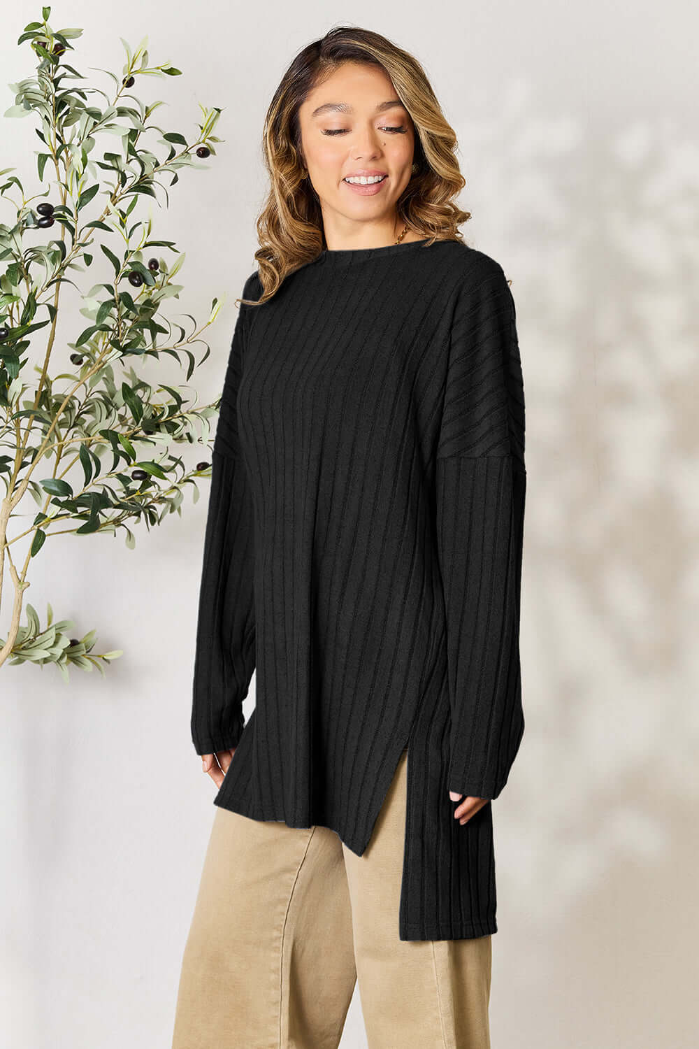 Model wearing a black ribbed long sleeve slit top paired with light beige pants, showcasing a stylish high-low design.