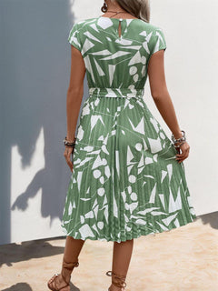 Back view of a Tied Pleated Printed Cap Sleeve Dress in green with abstract white patterns, showcasing pleats and a belted waist.