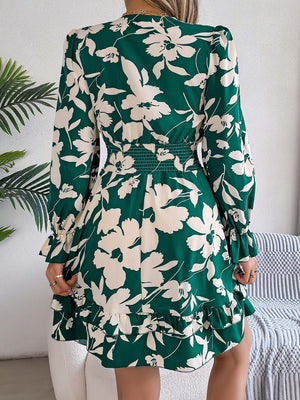 Back view of a woman wearing a green floral long sleeve dress with ruffles and a tied waist.